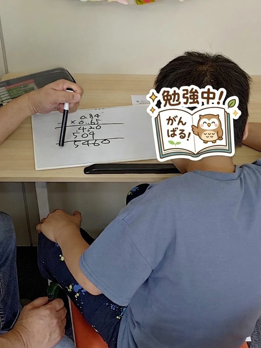 帯広東教室 個別学習支援 — ホワイトボードで小数の掛け算 (0.84 × 0.65) の筆算に取り組む子ども、スタッフが隣で見守り (帯広市 学習支援特化型 児童発達支援・放課後等デイサービス)